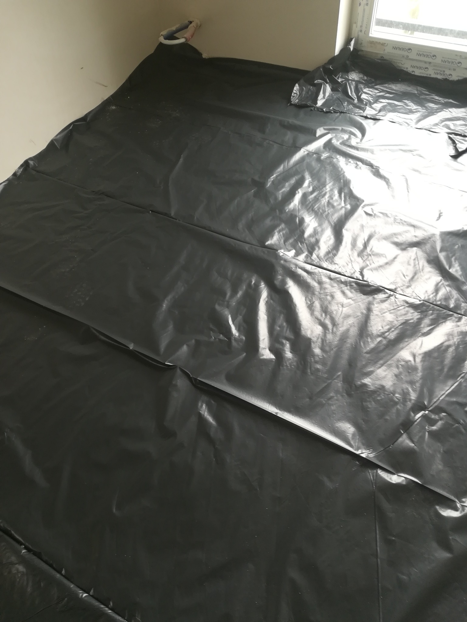 Przygotowanie do wylewki: folia ochronna rozłożona na podłodze w pomieszczeniu z oknem.