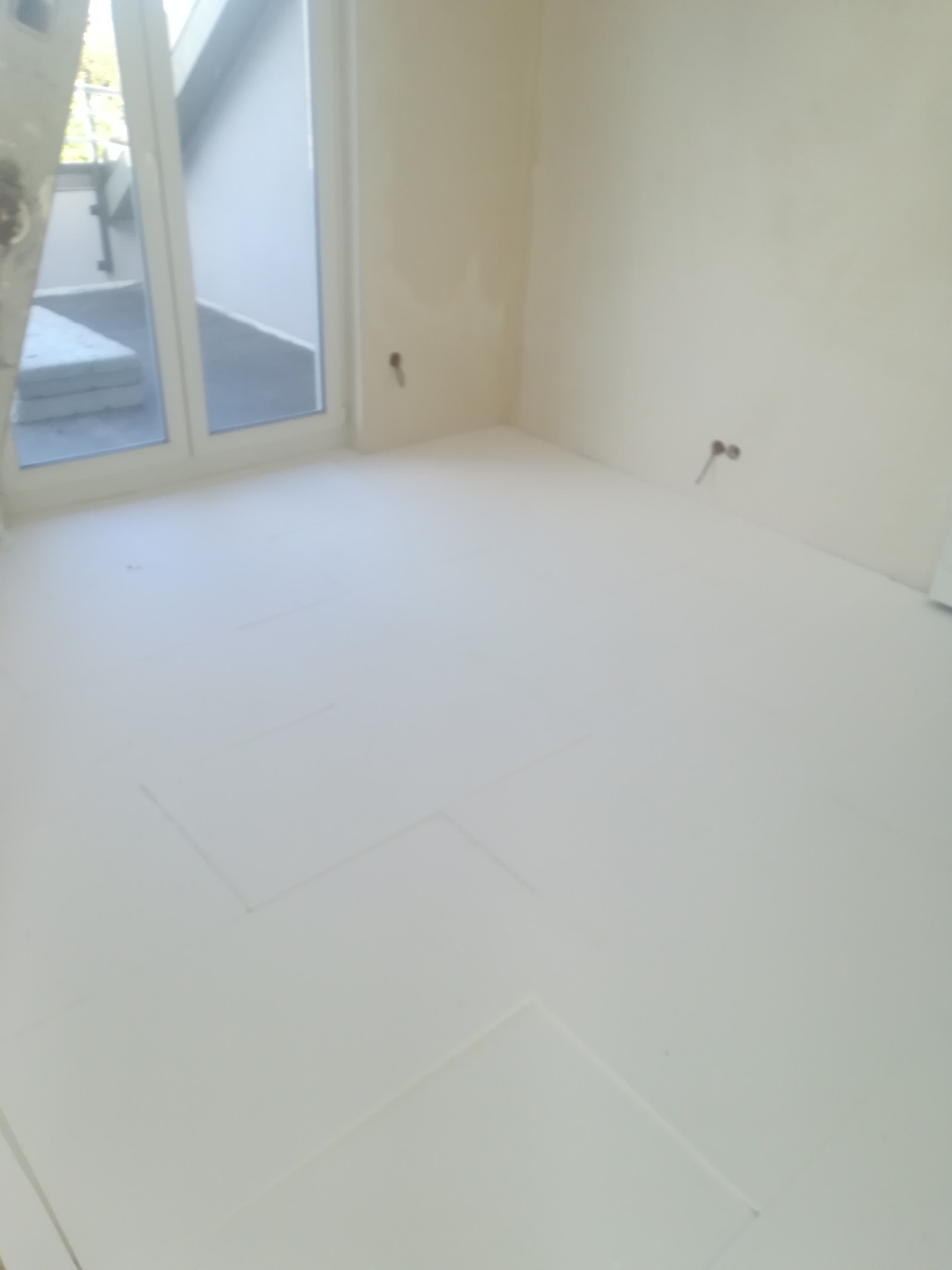 Białe płyty izolacyjne ułożone na podłodze w pomieszczeniu z oknem balkonowym, przygotowane pod wylewkę jastrychową.