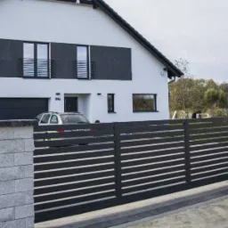 Nowoczesna brama przesuwna z poziomych profili, zamontowana przed domem z garażem i elementami w kolorze antracytowym, widoczna z zewnątrz posesji.