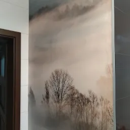 Fototapeta z motywem mglistego lasu w łazience, widoczna przy białych płytkach i brązowej futrynie drzwi.