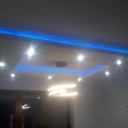 Sufit podwieszany z oświetleniem LED w kolorze niebieskim i punktowymi lampami, widoczny nowoczesny żyrandol i fragment okna.