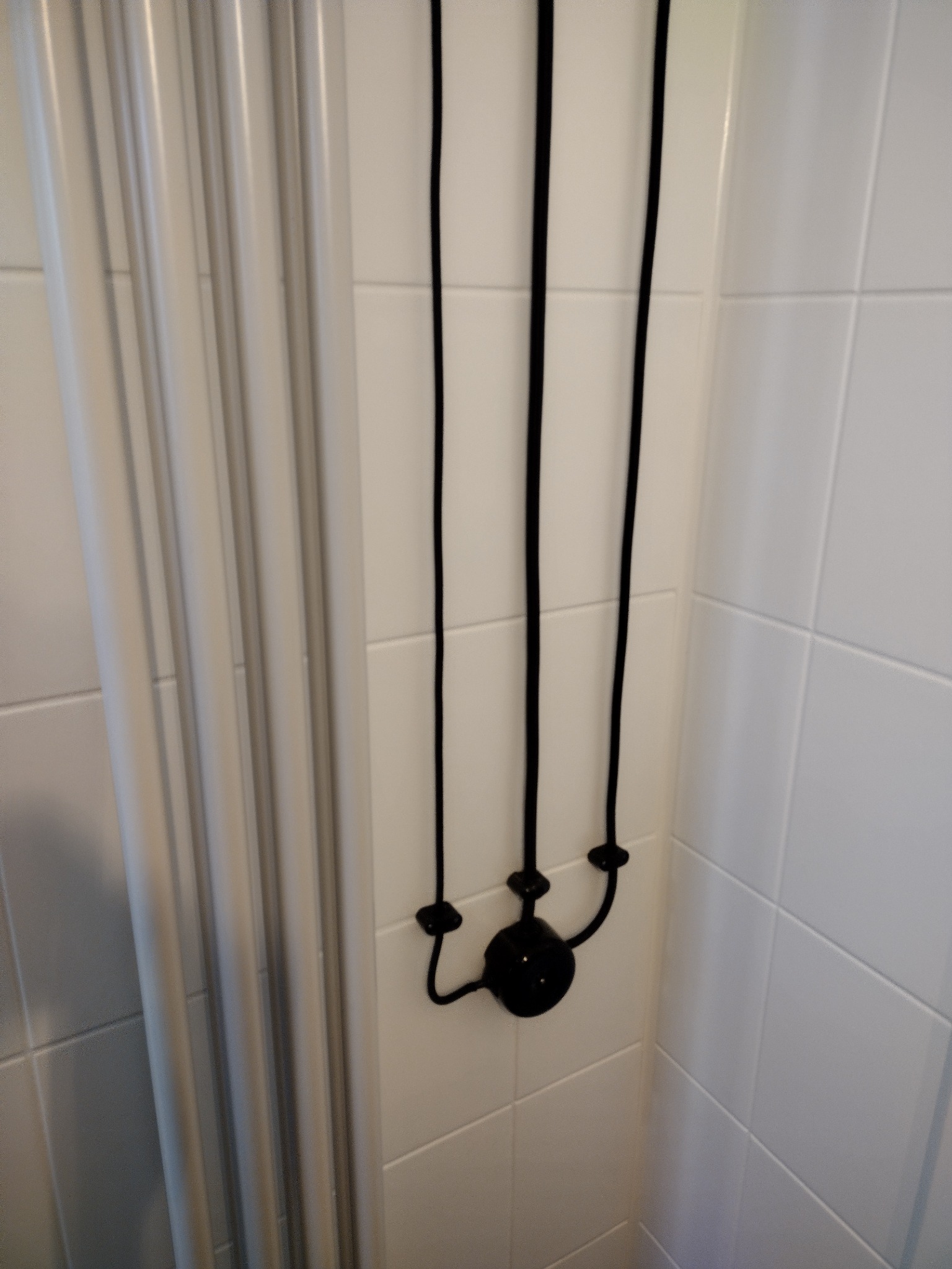 Biała łazienka z grzejnikiem drabinkowym i nietypowym czarnym oświetleniem wiszącym na ścianie z białych płytek.