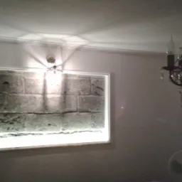 Oświetlona ściana z efektem cegieł w ramie, z żyrandolem w stylu vintage i wentylatorem pod sufitem.