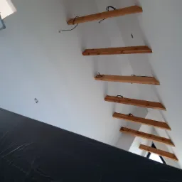 Poddasze w trakcie ocieplania, widoczne drewniane belki konstrukcyjne, przewody elektryczne i czarna folia ochronna zabezpieczająca przed zabrudzeniem podczas prac.