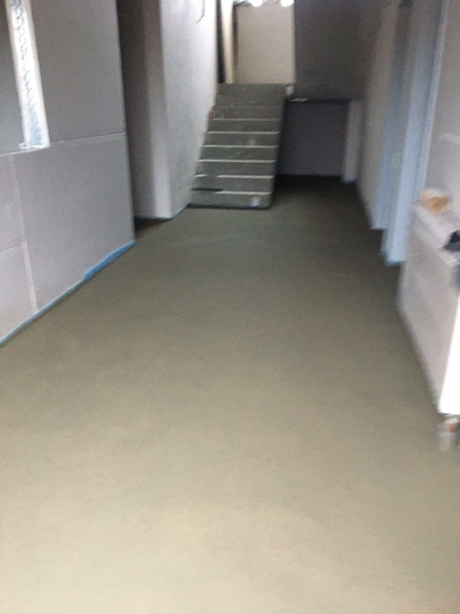 Świeżo wylana, jasnoszara posadzka w surowym wnętrzu z widocznymi schodami i przygotowanymi ścianami.