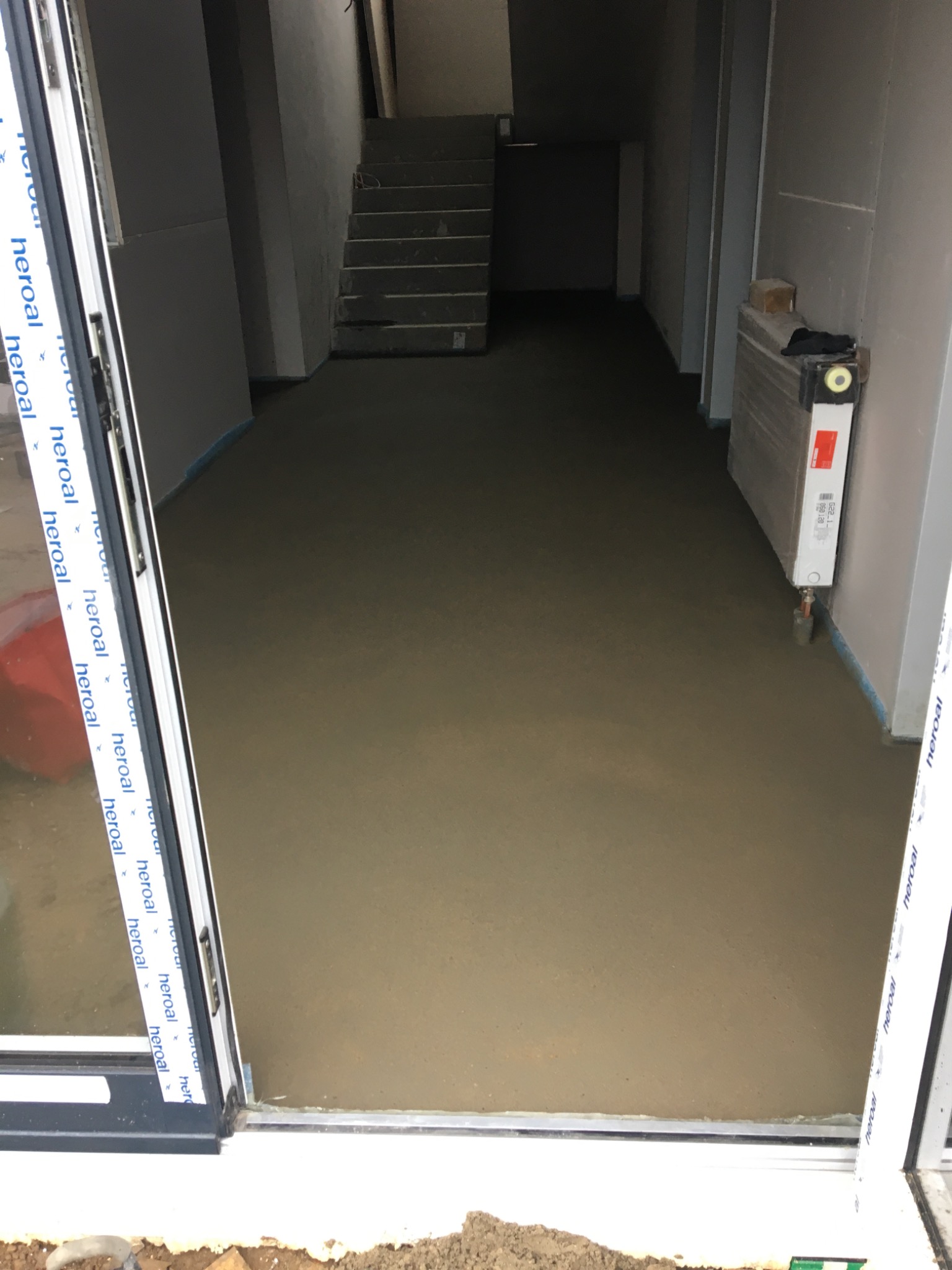 Świeżo wylana, gładka posadzka jastrychowa w surowym wnętrzu, widok zza otwartych drzwi balkonowych z profilem Heroal.