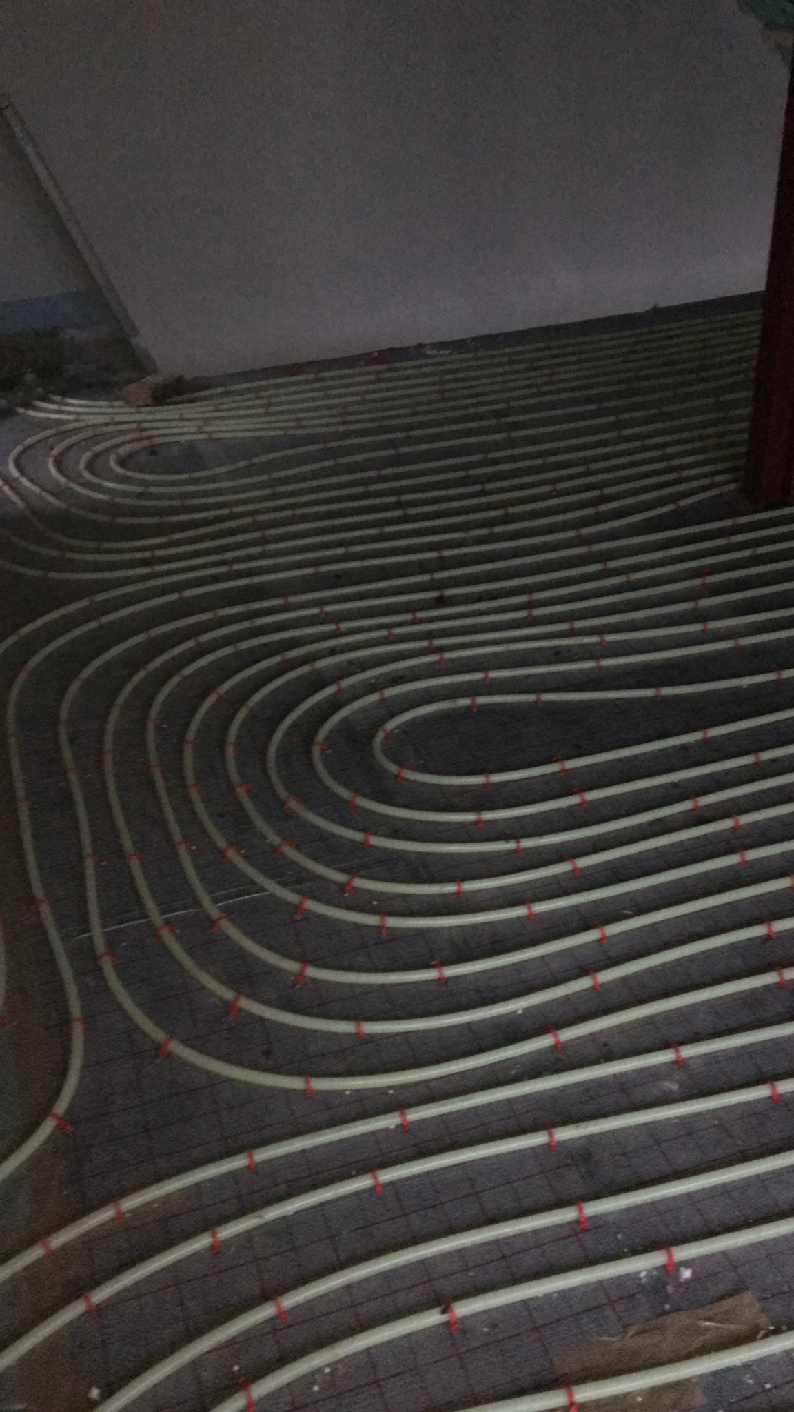 Układanie rur ogrzewania podłogowego w pętli na siatce z czerwonymi mocowaniami przed wylaniem jastrychu.