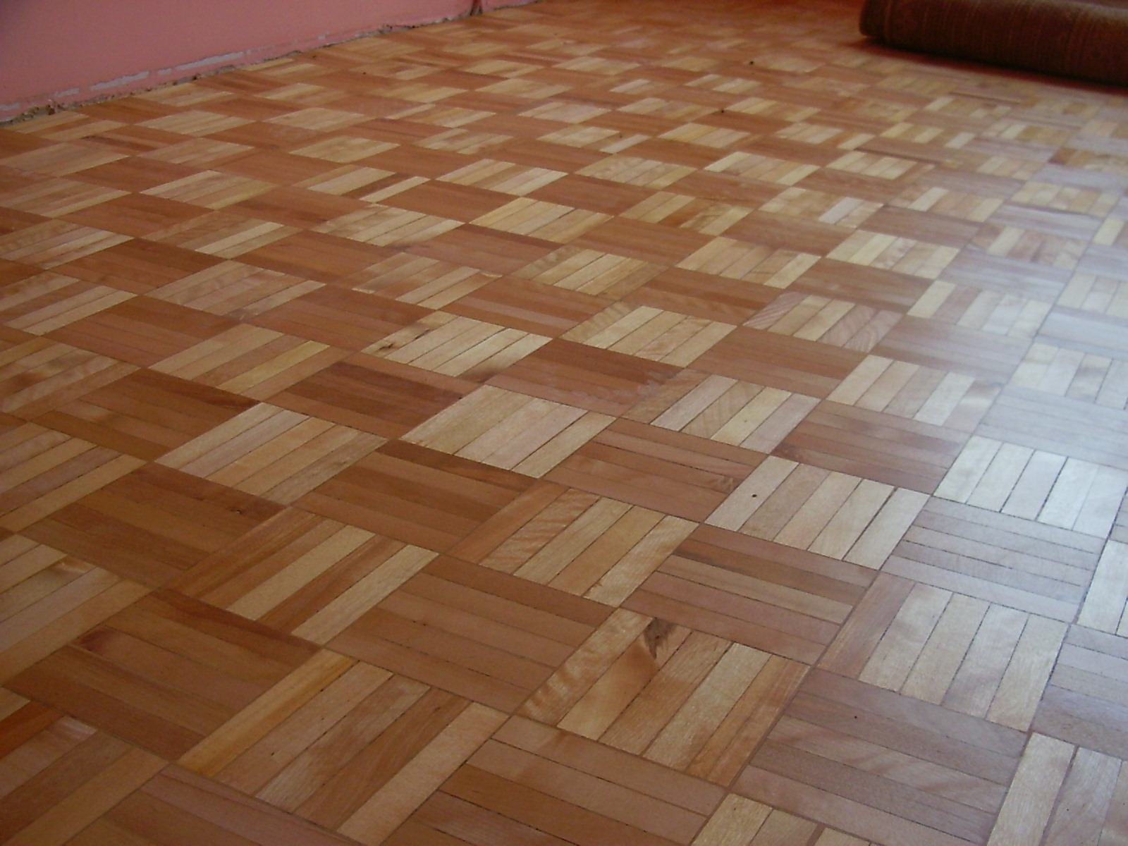 Parkiet ułożony w kwadraty z drewna o różnych odcieniach, widoczne delikatne refleksy światła na powierzchni.