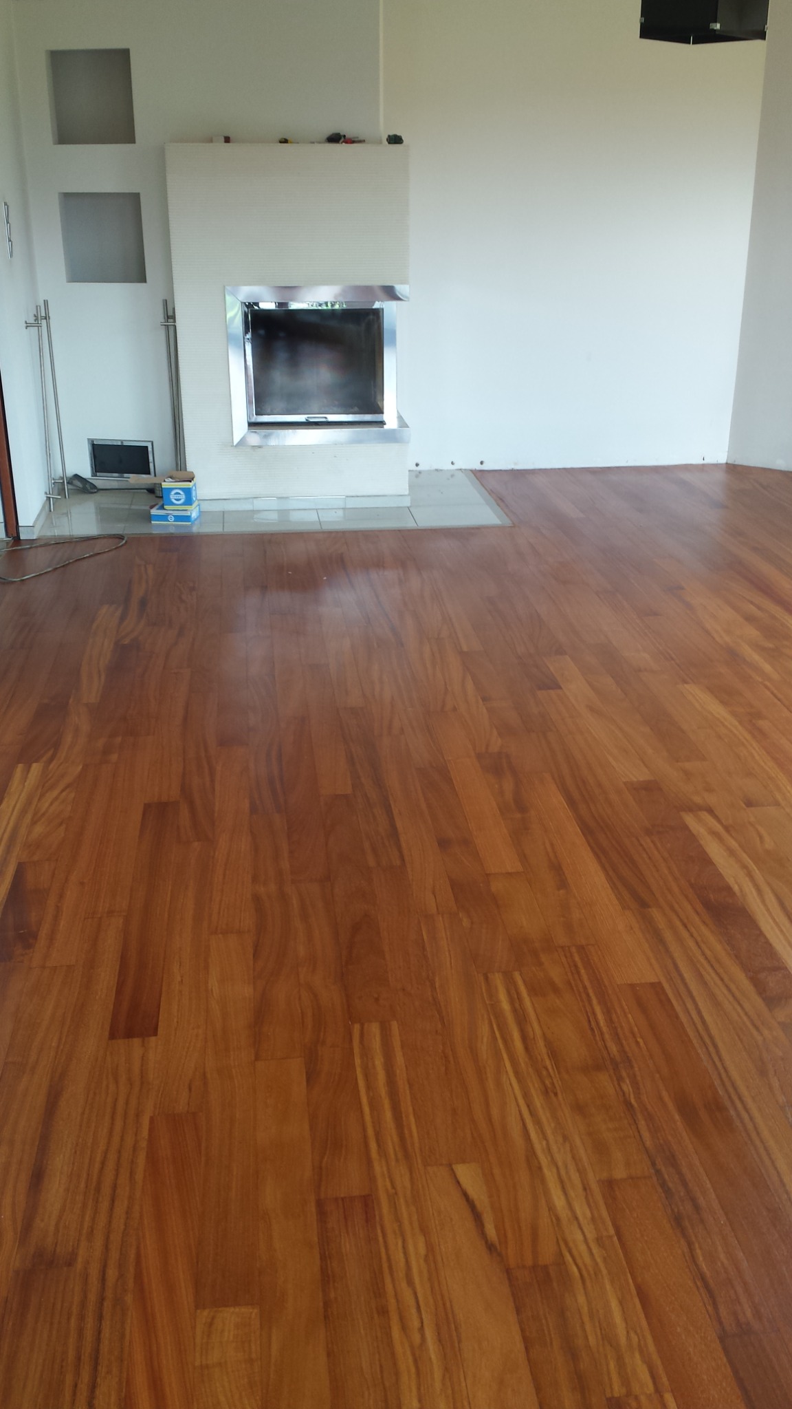 Ułożony parkiet z egzotycznego drewna w pomieszczeniu z kominkiem o nowoczesnej obudowie, widoczne ślady po wierceniu w ścianie.