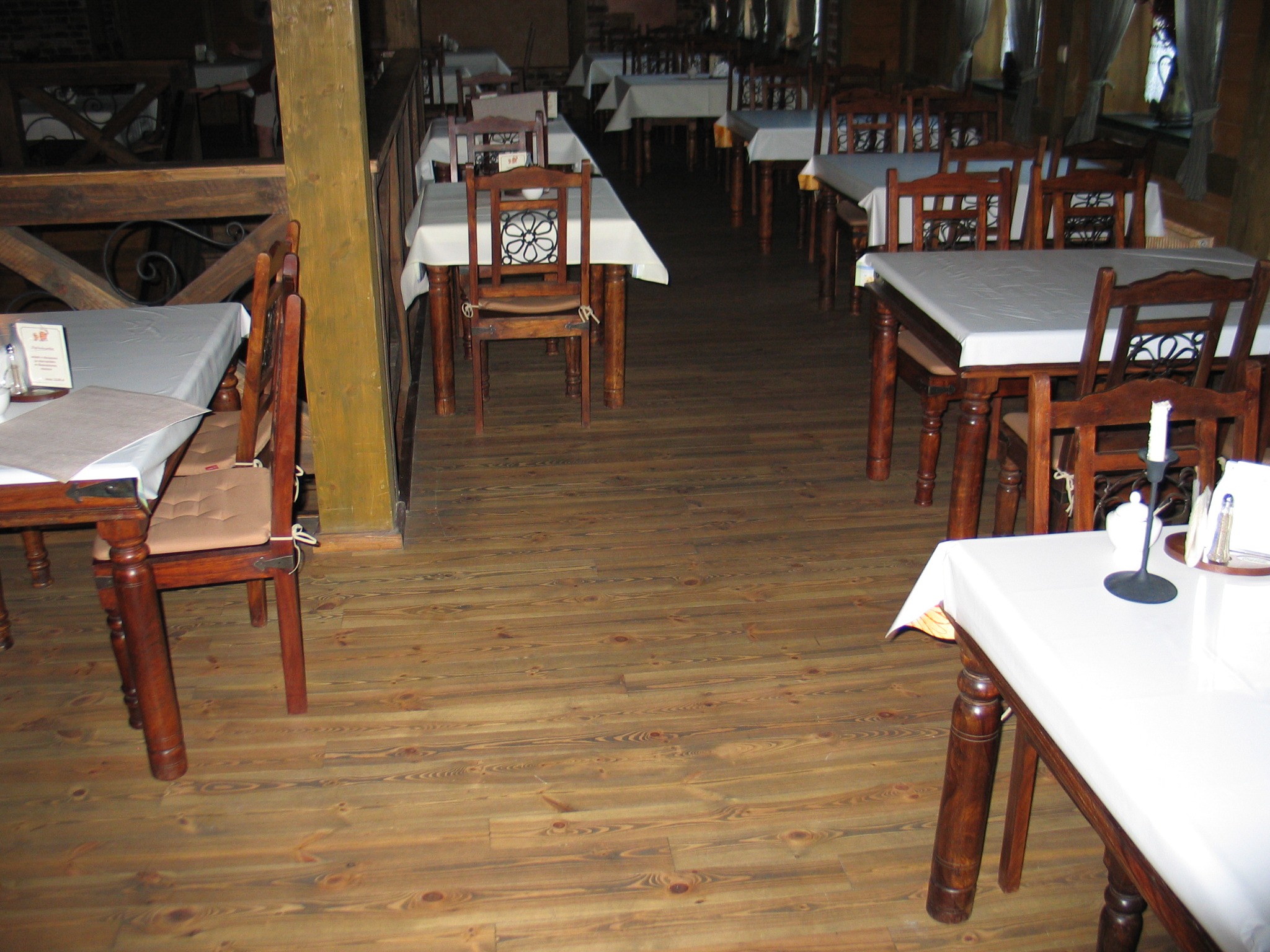 Wykończona podłoga z desek w restauracji z drewnianymi stolikami nakrytymi białymi obrusami, widoczne sęki i usłojenie drewna.