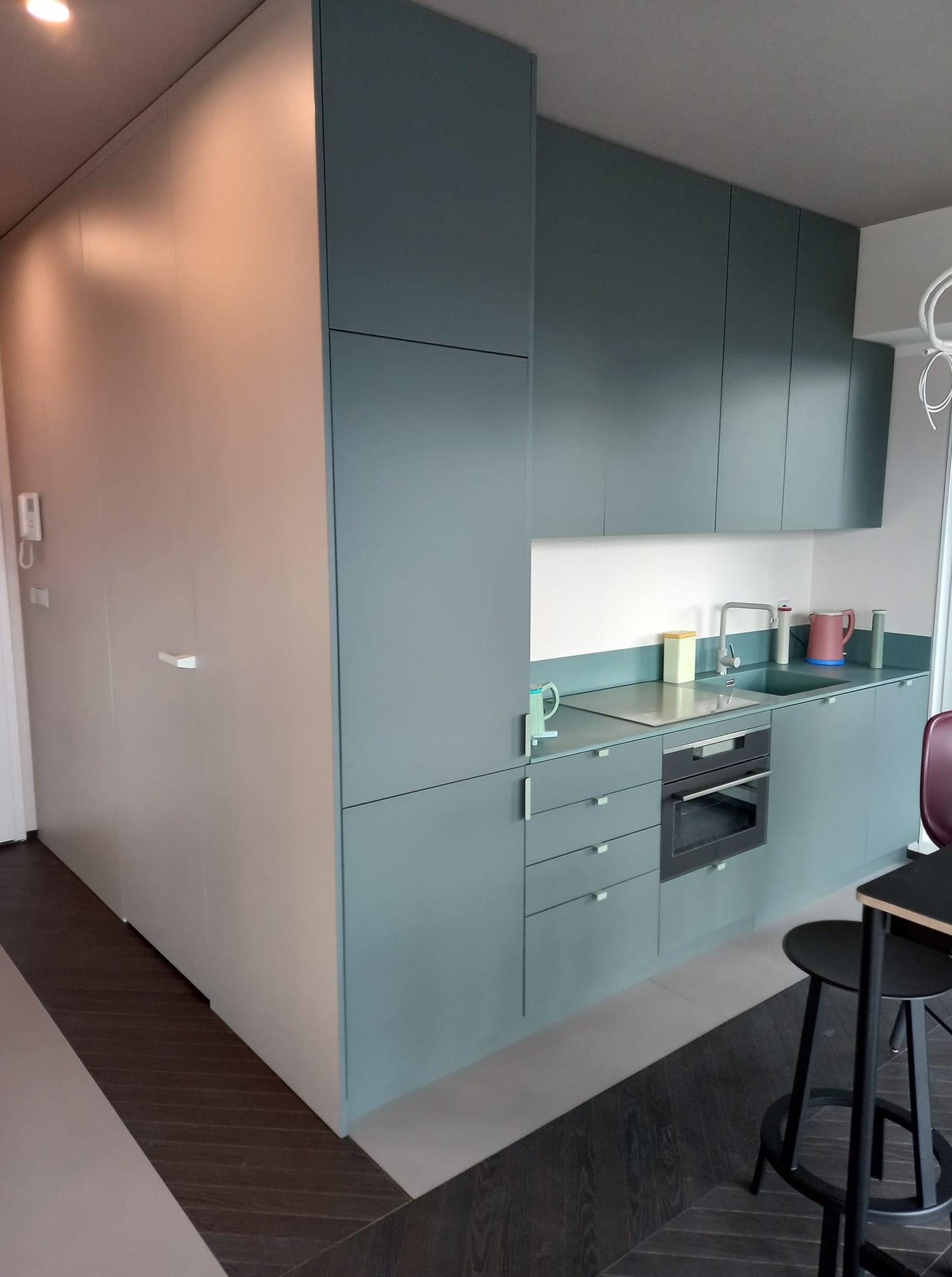 Nowoczesna kuchnia z zabudową w odcieniach szarości i bieli. Minimalistyczny design, ciemna podłoga w jodełkę, wysoki słupek i szafki wiszące.