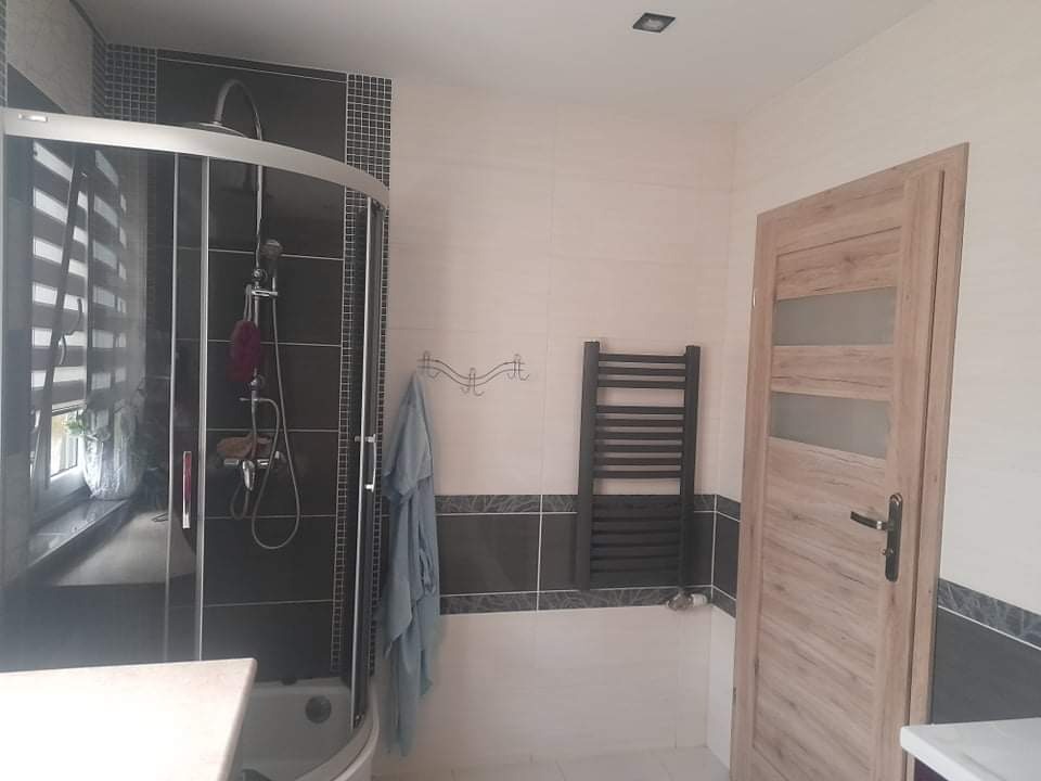 Wykończona łazienka z kabiną prysznicową z czarnymi elementami, grzejnikiem drabinkowym i drewnianą stolarką drzwiową.