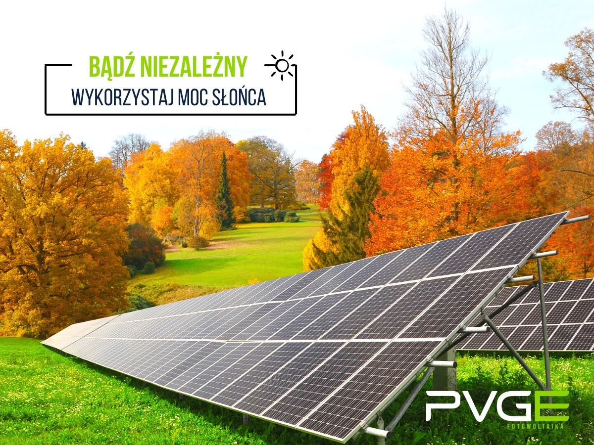 Instalacja paneli słonecznych na zielonej łące z jesiennym lasem w tle, z hasłem reklamowym 'Bądź niezależny. Wykorzystaj moc słońca' i logo firmy PVGE Fotowoltaika.