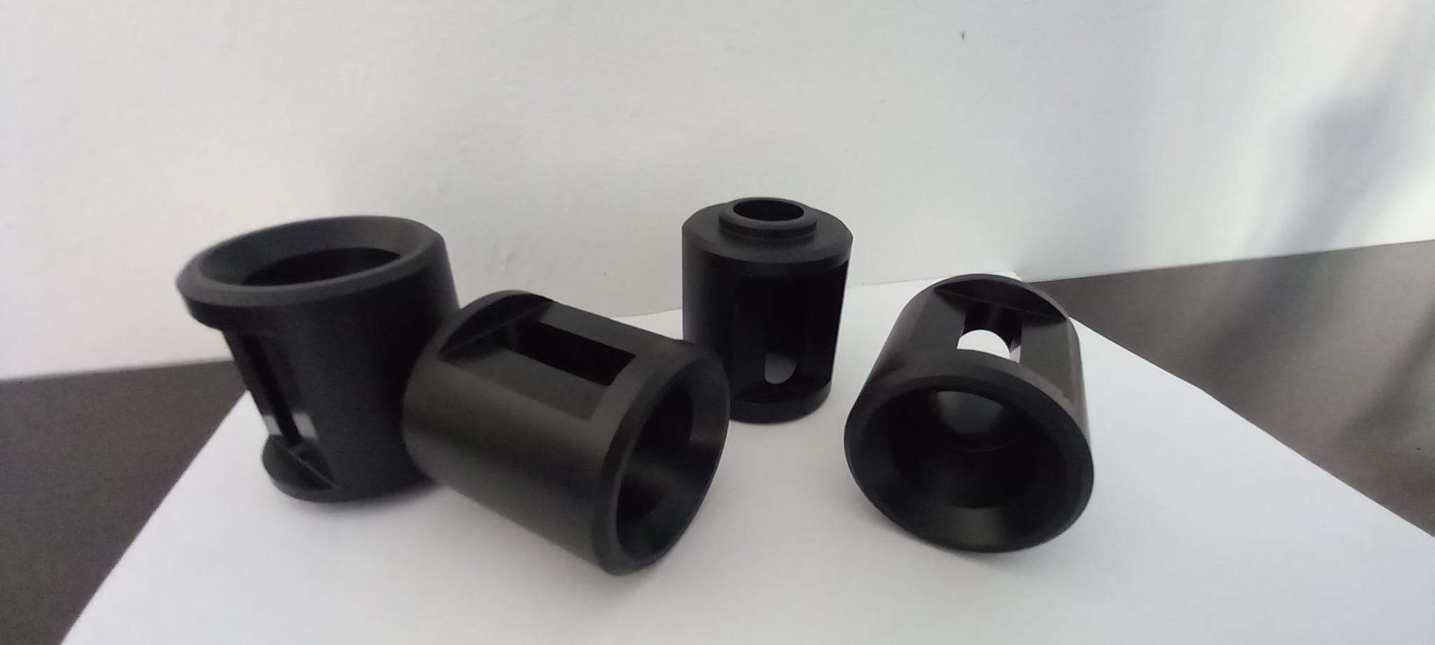 Czarne, precyzyjnie wykonane elementy z tworzywa sztucznego lub metalu, o cylindrycznych kształtach z różnymi otworami i wycięciami, ułożone na białym tle, prezentujące dokładność obróbki.