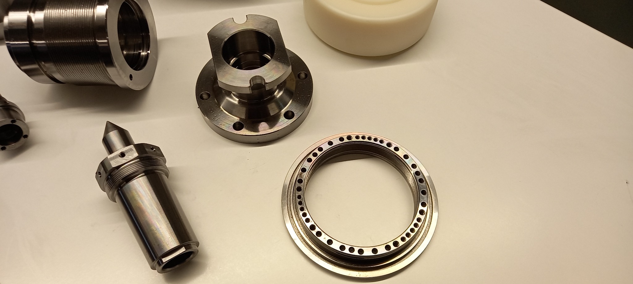 Precyzyjnie wykonane, metalowe elementy maszyn, w tym tuleje z gwintem, pierścienie z otworami i kołnierze, leżące na jasnym blacie.
