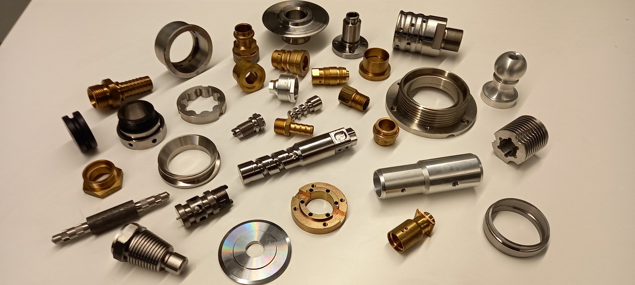Zestaw różnorodnych, precyzyjnie wykonanych metalowych elementów i komponentów, w tym gwintowane złączki, tuleje, pierścienie i wałki, ułożonych na jasnym tle, prezentujących różne etapy obróbki...