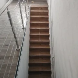 Schody wyłożone brązowymi płytkami imitującymi drewno, z metalową balustradą, widok z góry.