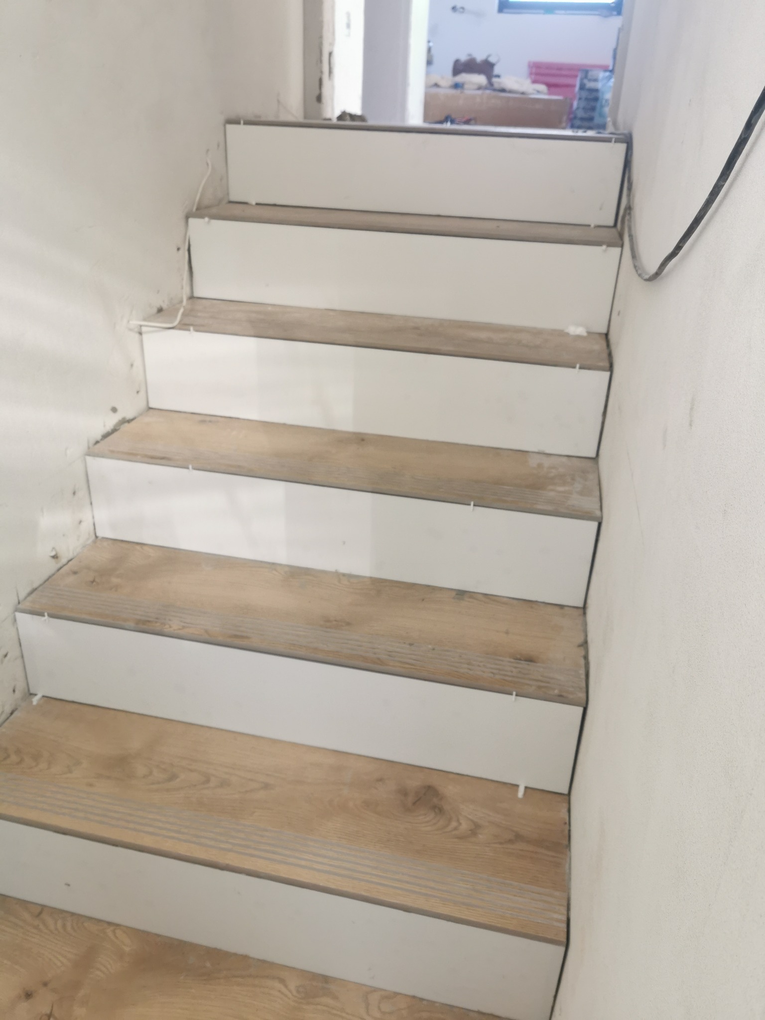 Montaż drewnopodobnych płytek na schodach w Piekoszowie, widoczne białe listwy wykończeniowe i krzyżyki dystansowe.