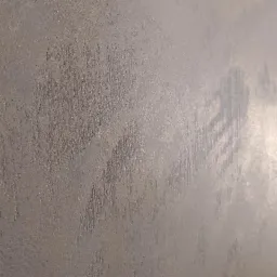 Ściana pokryta dekoracyjną, metaliczną farbą w odcieniach szarości z widoczną fakturą pionowych pociągnięć pędzla, tworząca efekt subtelnego cieniowania.