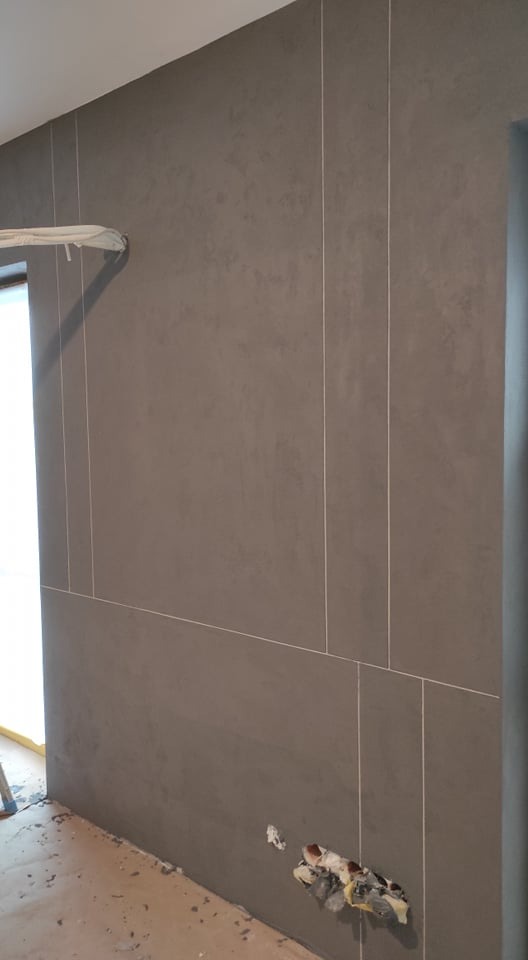 Ściana pokryta szarą, strukturalną masą z dekoracyjnymi pionowymi i poziomymi liniami, widoczne niedoskonałości w okolicy gniazdka elektrycznego.