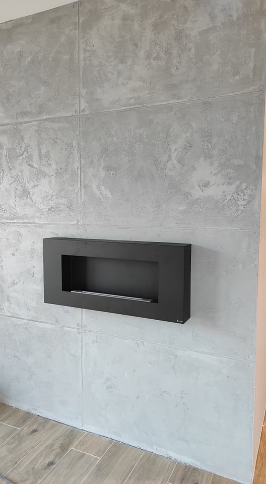 Ściana wykończona szarym tynkiem dekoracyjnym imitującym beton, z zamontowanym czarnym biokominkiem.