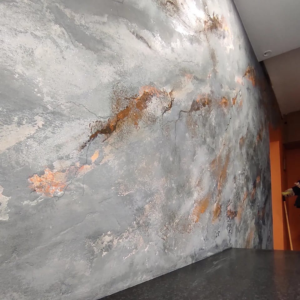 Dekoracyjna ściana z efektem betonu i rdzawymi smugami, widoczne delikatne pęknięcia w strukturze.