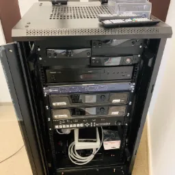 Szafa rack z zamontowanym sprzętem audio, w tym wzmacniacze Crown, odtwarzacz Panasonic, mikrofony AKG D7 w pudełkach i pilot, zainstalowana przez firmę z Lubina.