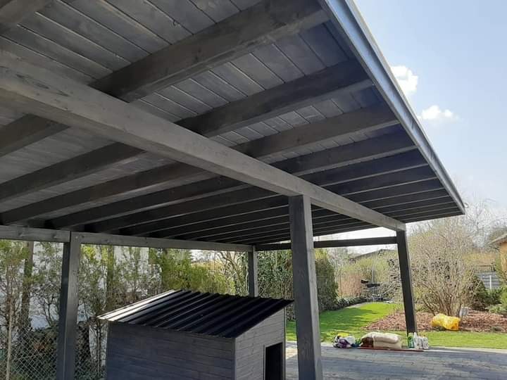 Zadaszenie tarasowe z ciemnego drewna, widok od dołu, z małym domkiem dla dzieci w tle, na lekko pochylonym podłożu z kostki brukowej.