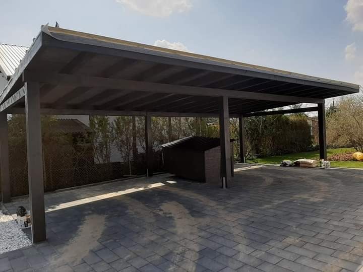 Zadaszenie na samochody z ciemnego drewna, widok z zewnątrz, z kostką brukową i zielenią w tle.