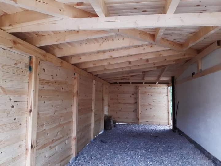 Wnętrze drewnianej konstrukcji w trakcie budowy, widoczne surowe deski ścian i dachu, podłoże wysypane żwirem, surowy stan wykończenia.