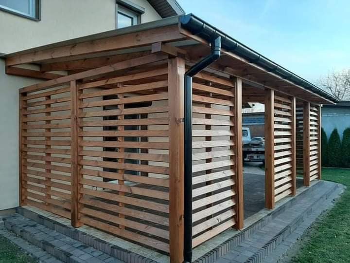 Zadaszona konstrukcja z drewnianymi lamelami, prawdopodobnie wiata lub zadaszenie tarasu, z widocznym systemem rynnowym i częściowo widocznym samochodem w tle.