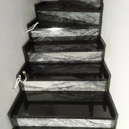 Schody wewnętrzne z czarnego kamienia z wyraźnym, szaro-białym wzorem żyłkowania na stopniach, widok z góry, widoczne wystające kable elektryczne ze ściany.