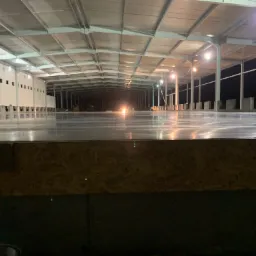 Wnętrze hali przemysłowej z nową, błyszczącą posadzką. Widoczne oświetlenie i konstrukcja dachu. Perspektywa z poziomu podłoża.