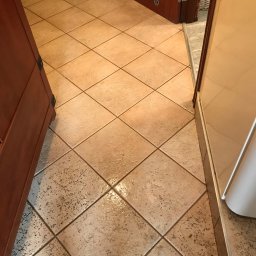 Perfect-Anna Łojeczko - Beżowa podłoga z płytek ułożonych w karo, widoczny fragment brązowych drzwi i szafki, jasne ściany.