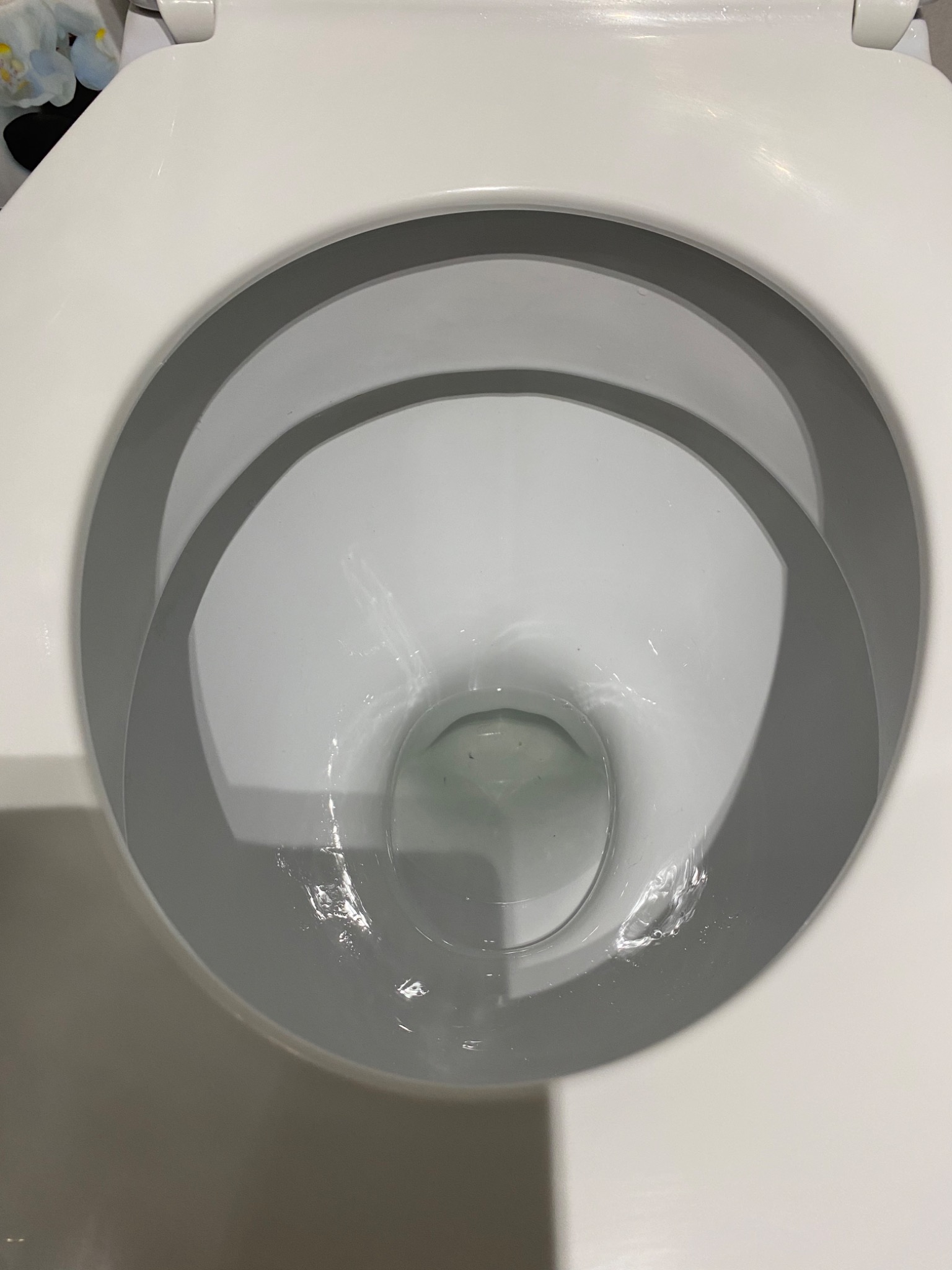 Wnętrze białej, ceramicznej muszli klozetowej wypełnionej czystą wodą, widok z góry.