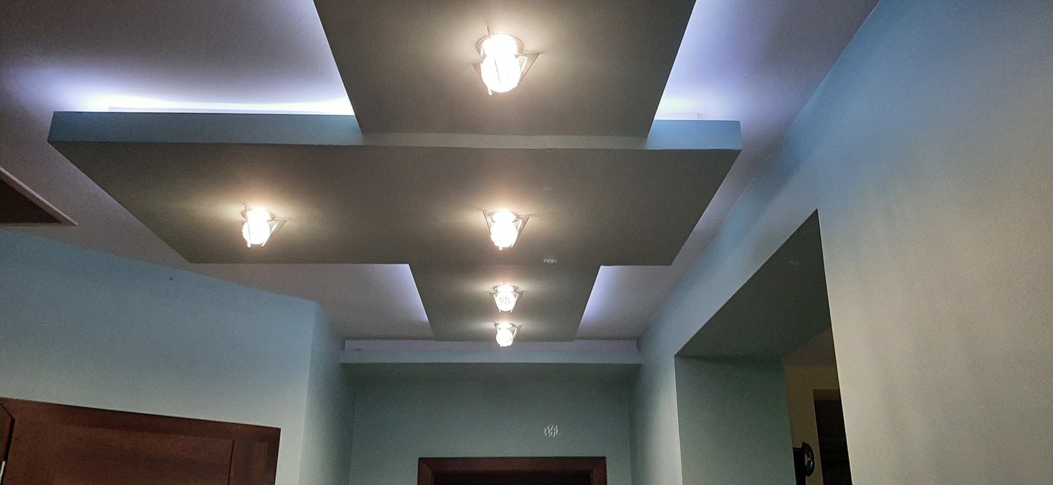 Nowoczesny sufit podwieszany z wbudowanym oświetleniem punktowym, tworzący geometryczny wzór na tle jasnych ścian.