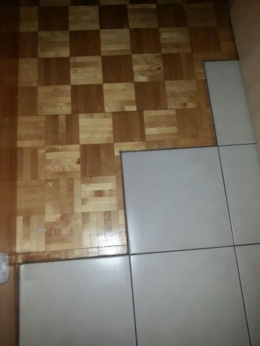 Fragment podłogi z parkietu ułożonego w szachownicę, sąsiadujący z ułożonymi jasnymi, kwadratowymi płytkami ceramicznymi. Widoczny etap prac wykończeniowych.