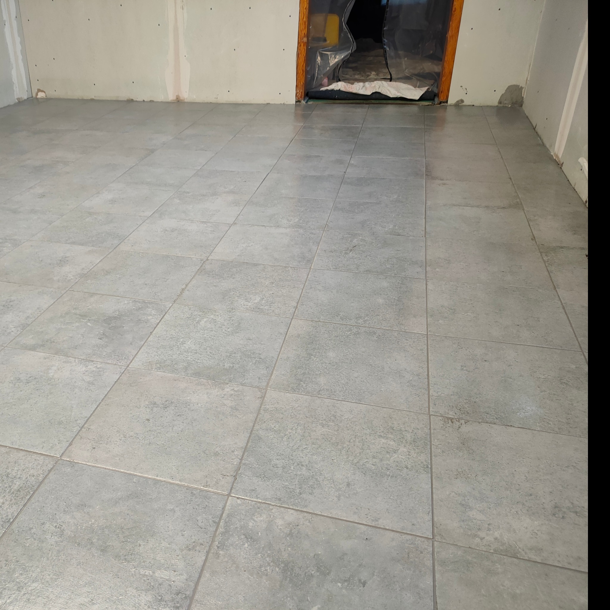 Świeżo położona, jasnoszara podłoga z płytek w pomieszczeniu w trakcie remontu, widoczne zabezpieczone folią drzwi.
