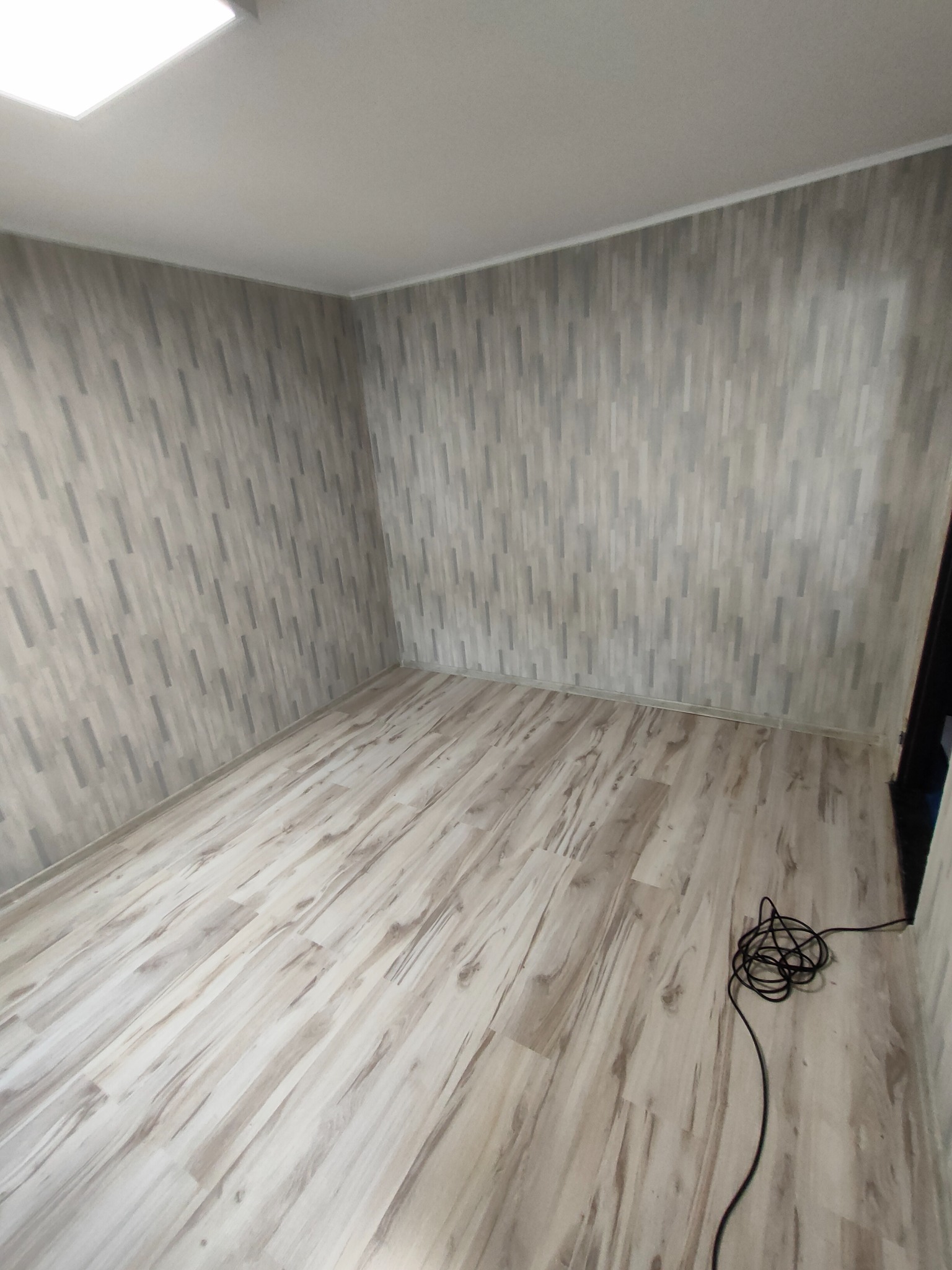 Pusty pokój po remoncie w Lipnie, z panelami podłogowymi imitującymi drewno i tapetą na ścianach. Widoczny kabel leżący na podłodze.