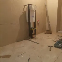 Montaż stelaża podtynkowego WC marki Roca w surowym wnętrzu łazienki, widoczne narzędzia i poziomica, ściany w trakcie przygotowania do wykończenia.