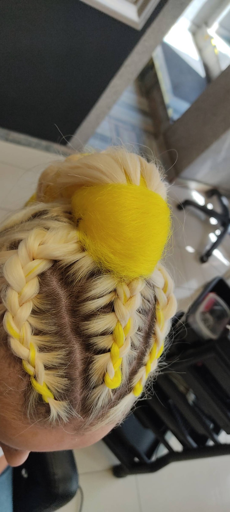 Blond włosy zaplecione w warkocze z żółtymi akcentami i żółtym pomponem na czubku głowy, widok z góry.