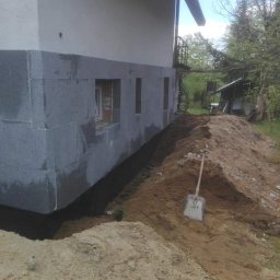 Celina kroenka - Budynek z szarej bloczków betonowych, widoczne okna w trakcie montażu, ziemia usypana wokół fundamentów, łopata oparta o pryzmę ziemi.