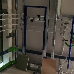 Wewnętrzna instalacja wodno-kanalizacyjna w trakcie montażu, widoczne rury PCV w kolorze niebieskim i białym, metalowe stelaże montażowe i elementy mocujące do ściany.