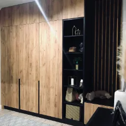 Duża szafa z drewnianymi frontami i czarnymi akcentami, z otwartymi półkami z dekoracjami, na podłodze wzorzysty dywan.