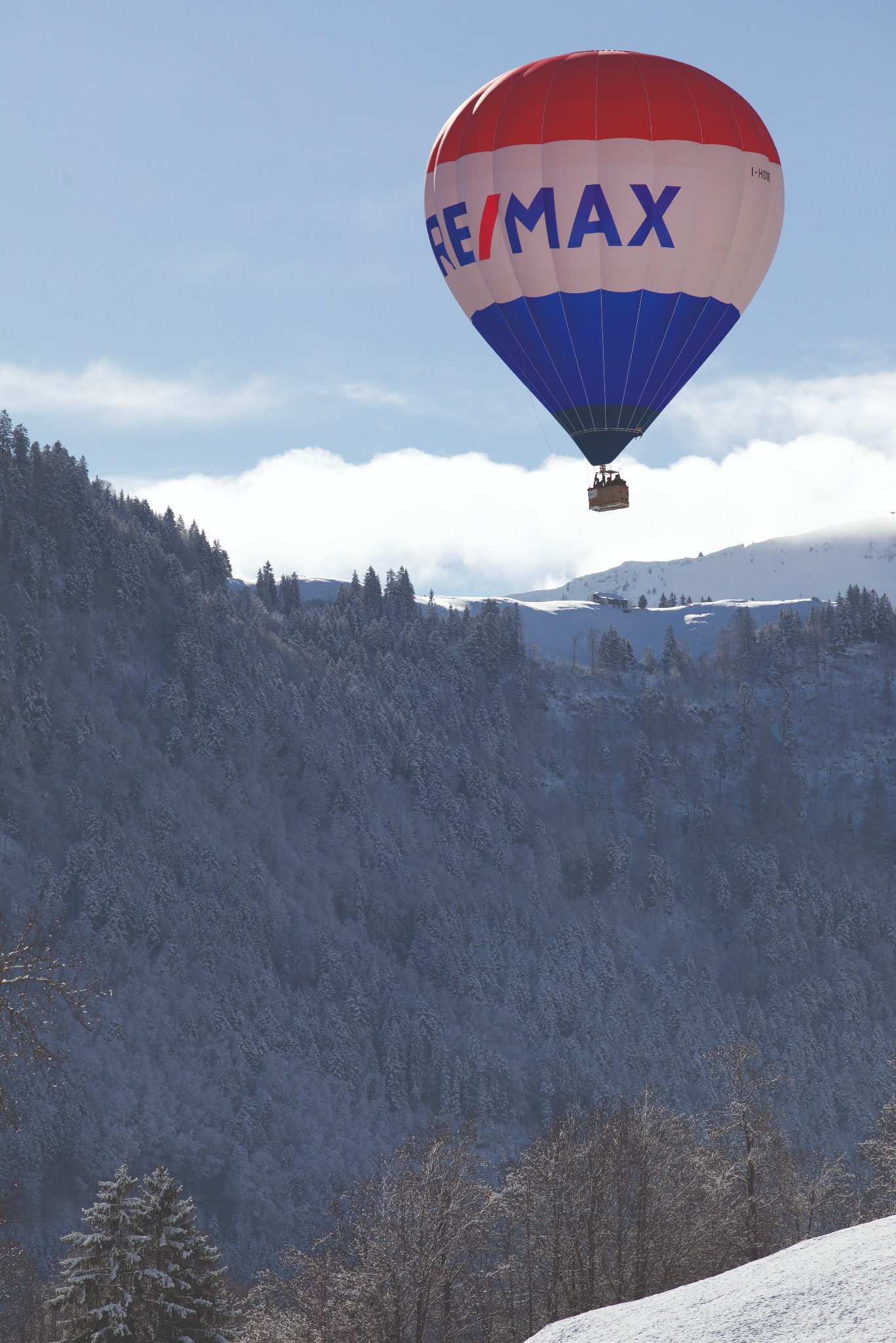 Kolorowy balon z logo RE/MAX na tle zaśnieżonych gór i błękitnego nieba.