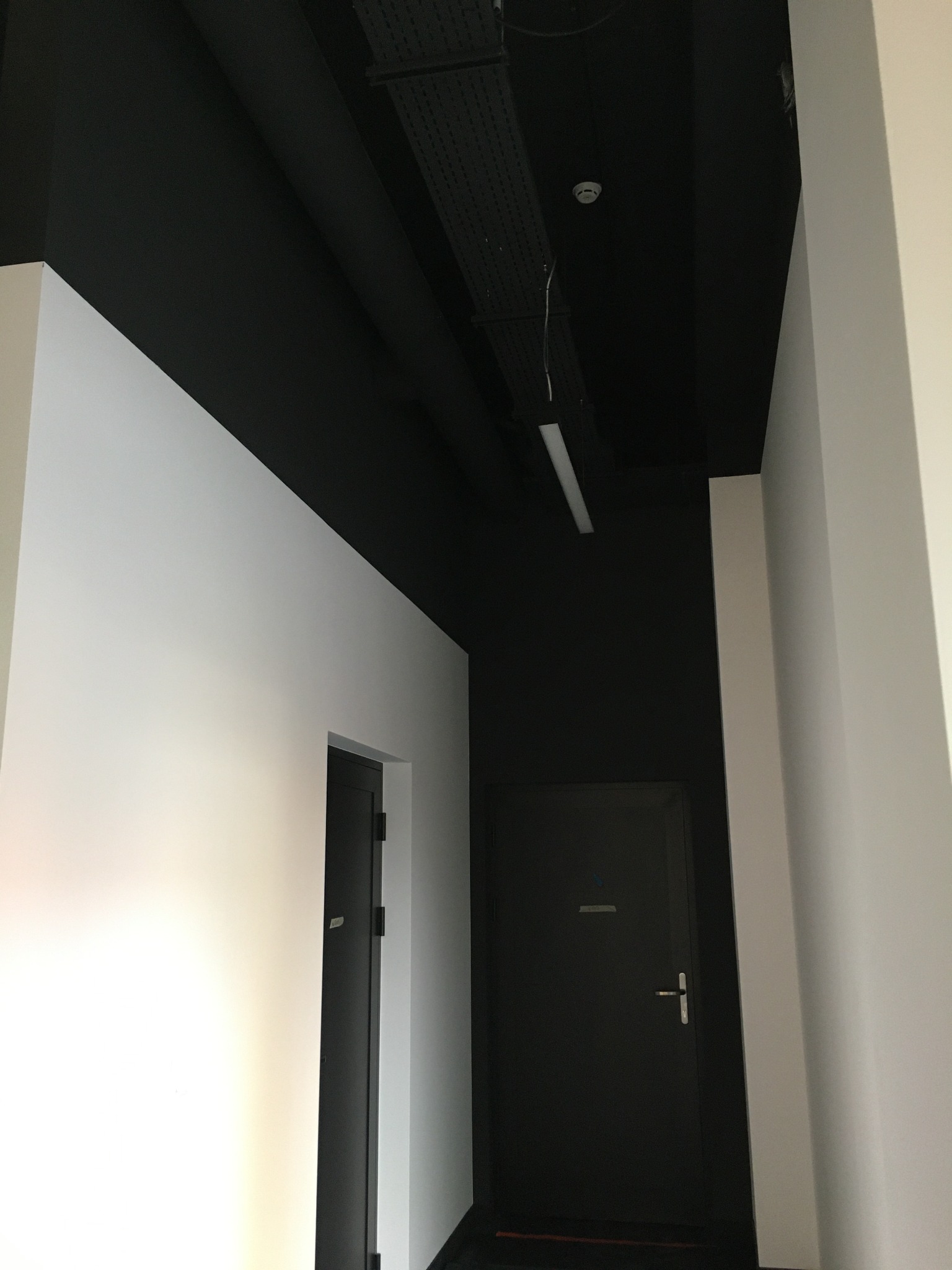 Wnętrze biura po remoncie: białe ściany kontrastują z czarnym sufitem, widoczne dwie ciemne drzwi i oświetlenie sufitowe.