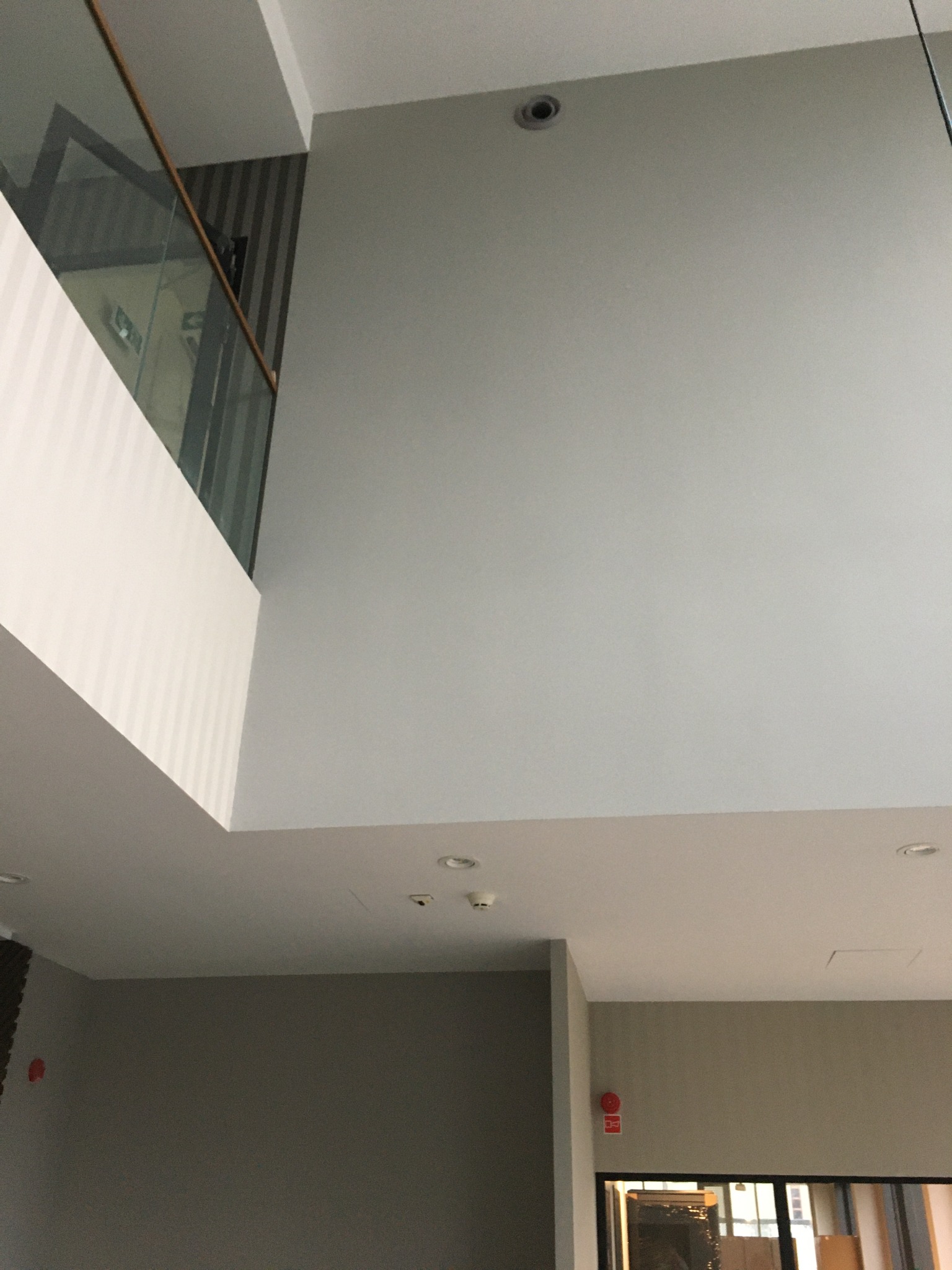 Wysokie, jasne wnętrze biurowe po odświeżeniu, widok na sufit z oświetleniem i fragment szklanej balustrady.