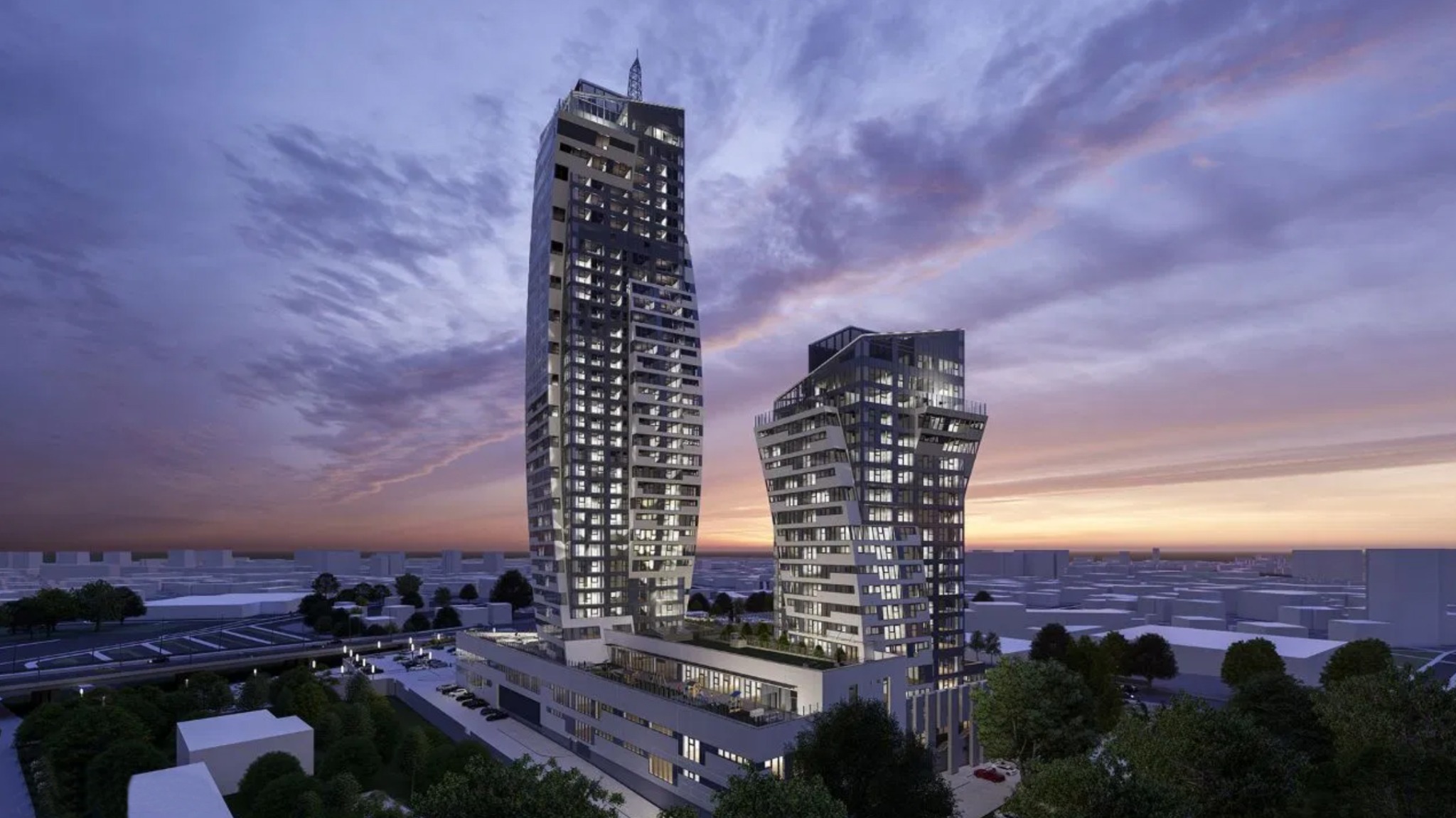 Dwa nowoczesne wieżowce o asymetrycznych bryłach, oświetlone wieczornym światłem, z widocznymi światłami w oknach, na tle zachodzącego słońca i zurbanizowanego krajobrazu.