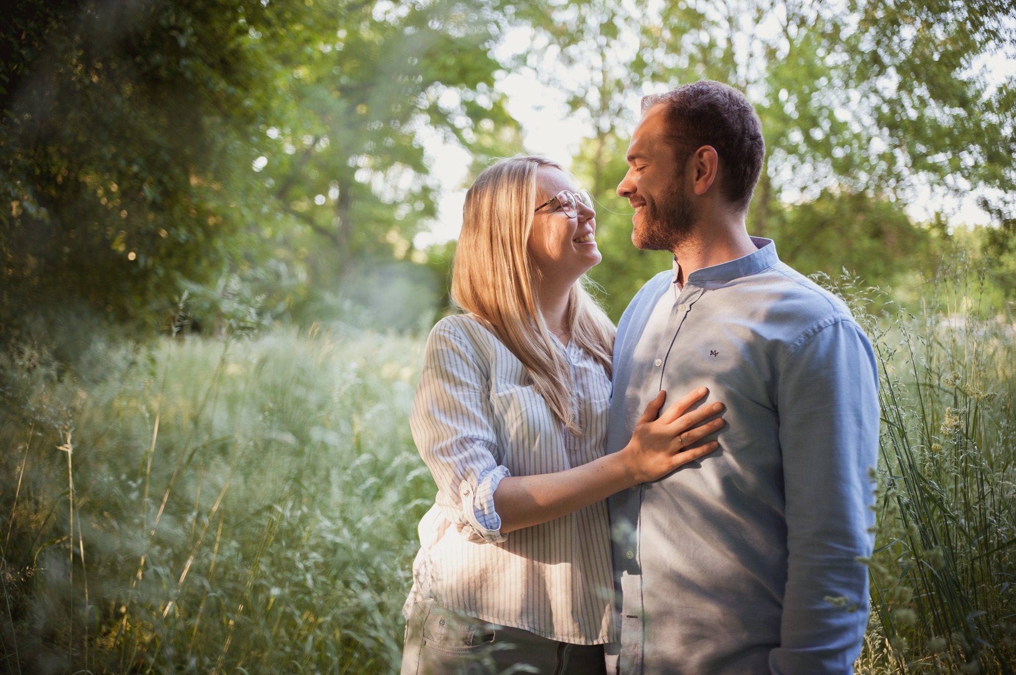 Zakochana para w zwiewnej scenerii łąki, ona w okularach dotyka jego piersi, oboje uśmiechnięci.