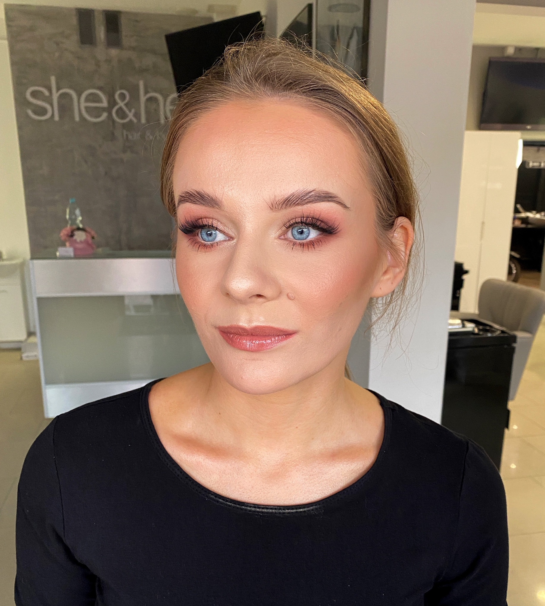 Portret kobiety z delikatnym, różowym cieniowaniem powiek i błyszczącymi ustami, wykonanym w salonie kosmetycznym.